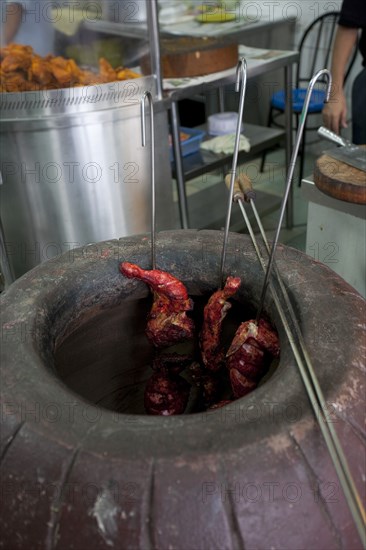 Malaysia, Kuala Lumpur, Skewered Tandoori chicken while being baked inside a Tandoor Oven at the front of an Indian restaurant.