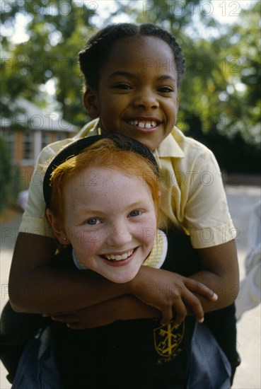 England, West Midlands, Birmingham, Smiling young girls in school playground with the white girl giving her black friend a piggy back.