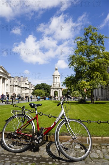 Ireland, County Dublin, Dublin City, Trinity College university with people walking through Parliament Square towards the Campanile with bicycles leaning against a chaon fence in the foreground.