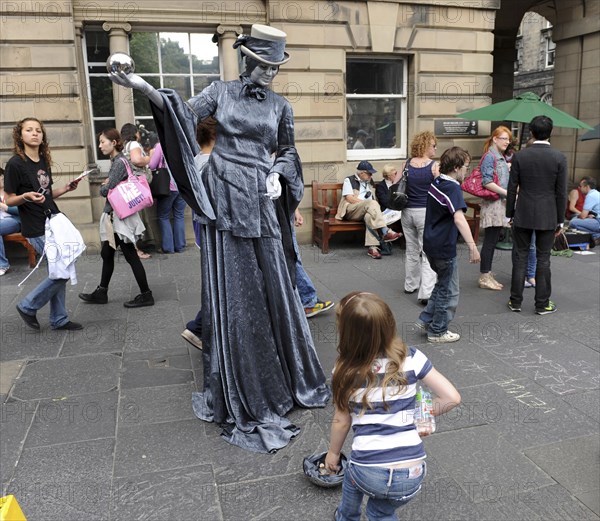 Scotland, Lothian, Edinburgh Fringe Festival of the Arts 2010, Street performers and crowds on the Royal Mile, mime performer with chrome sphere and child putting money in hat.