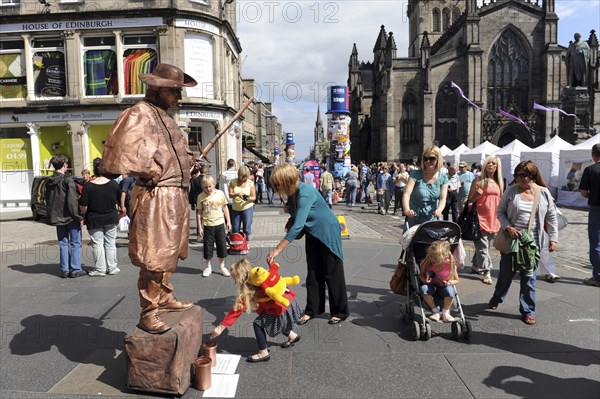 Scotland, Lothian, Edinburgh Fringe Festival of the Arts 2010, Street performers and crowds on the Royal Mile, mime performer with child putting money in a jar.