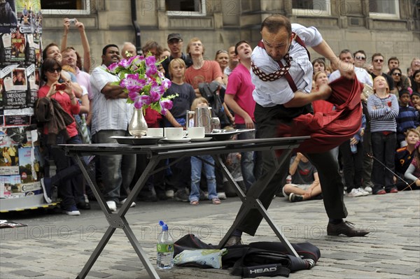 Scotland, Lothian, Edinburgh Fringe Festival of the Arts 2010, Street performers and crowds on the Royal Mile, magaician pulling table cloth from under plates.