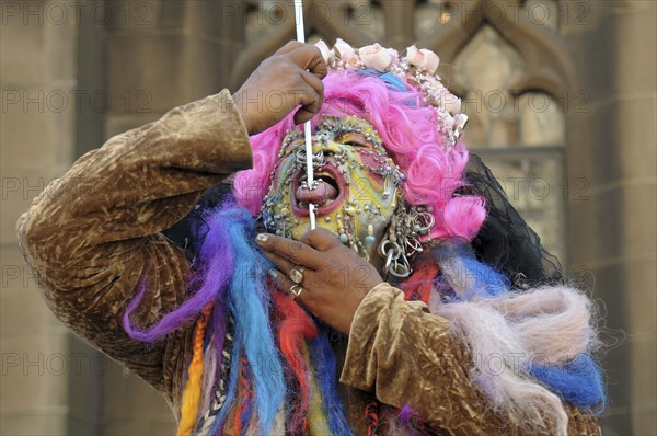 Scotland, Lothian, Edinburgh Fringe Festival of the Arts 2010, Street performers and crowds on the Royal Mile, mand with muliple facial piercings putting spike through his tongue.