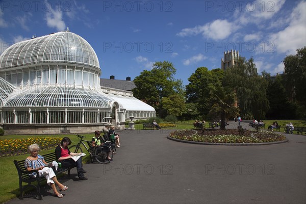 Ireland, Northern, Belfast, Botanic Gardens with people sat on benches outside the Palm House next to Queens University both designe by architect Charles Lanyon.