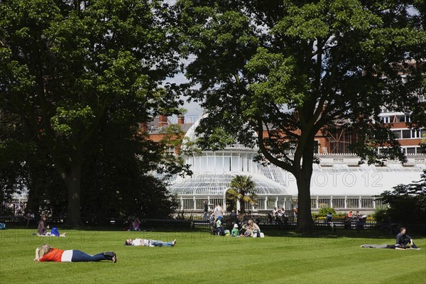 Ireland, Northern, Belfast, Botanic Gardens with people sat on benches outside the Palm House next to Queens University both designe by architect Charles Lanyon.