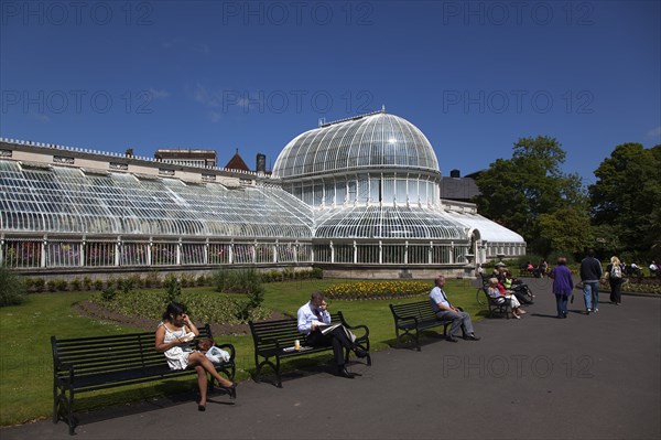 Ireland, Northern, Belfast, Botanic Gardens with people sat on benches outside the Palm House next to Queens University both designe by architect Charles Lanyon.