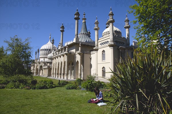 England, East Sussex, Brighton, The Royal Pavilion, 19th century retreat for the then Prince Regent, Designed by John Nash in a Indo Sarascenic style, girl reading in the foreground.