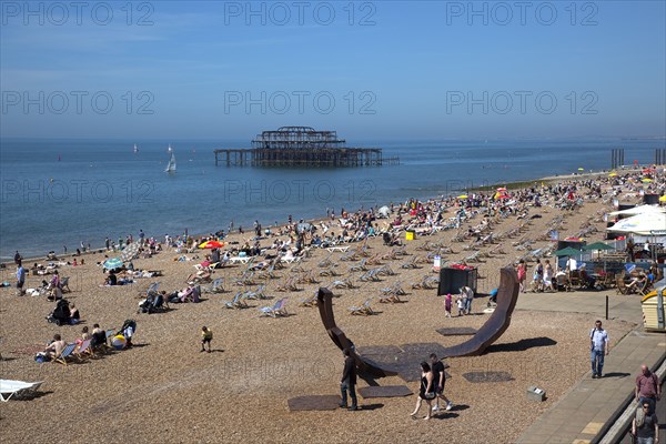 England, East Sussex, Brighton, view over the pebble beach with modern sculpture in the foreground and the burnt out ruins of the West Pier in the background.