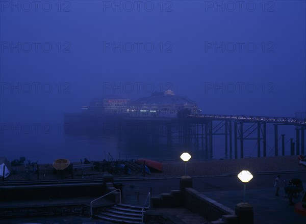 Brighton, East Sussex, England. The West Pier illuminated in evening light with mist on the sea European Great Britain Northern Europe UK United Kingdom Warm Light Water