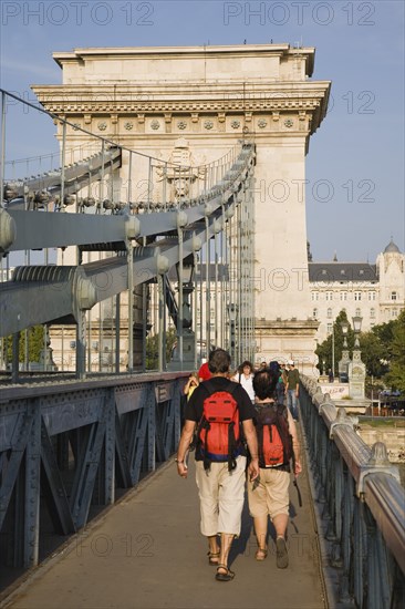 Budapest, Pest County, Hungary. Tourists with matching day packs crossing Szechenyi Chain Bridge or Memory Bridge over the River Danube on foot. Hungary Hungarian Europe European East Eastern Buda Pest Budapest City Architecture Bridge Transport Szechenyi Chain Memory Walking people Pedestrians Tourists Destination Destinations Eastern Europe Holidaymakers Tourism