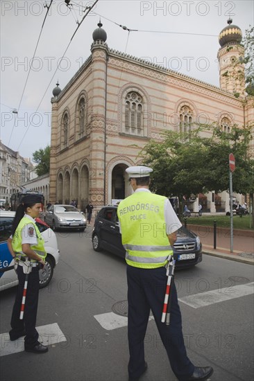Budapest, Pest County, Hungary. Hungarian traffic police wearing high visability jackets on road outside The Great Synagogue also known as Dohany Street Synagogue. Hungary Hungarian Europe European East Eastern Buda Pest Budapest City Dohany Street Great Synagogue Police Man Woman High Visability Jackets Bibs Vests Security Eastern Europe Female Women Girl Lady Male Men Guy Religion Religion Religious Judaism Jew Jews
