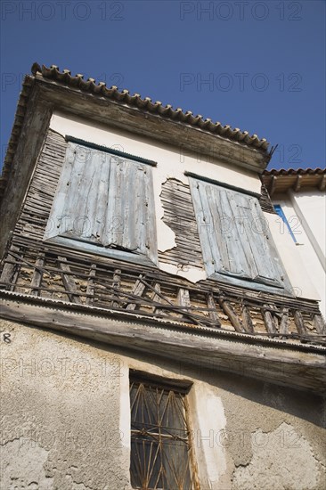 Samos Island, Northern Aegean, Greece. Vathy. Detail of old house with wooden window shutters and exposed timber frame view from below looking upwards. Greece Greek Europe European Vacation Holiday Holidays Travel Destination Tourism Ellas Hellenic Northern Agean Samos Island Vathy Architecture Details Exterior Facade Shuuters Shuttered Windows Decay Urban Run-down Dilapidated Ruin Blue Destination Destinations Ellada Southern Europe