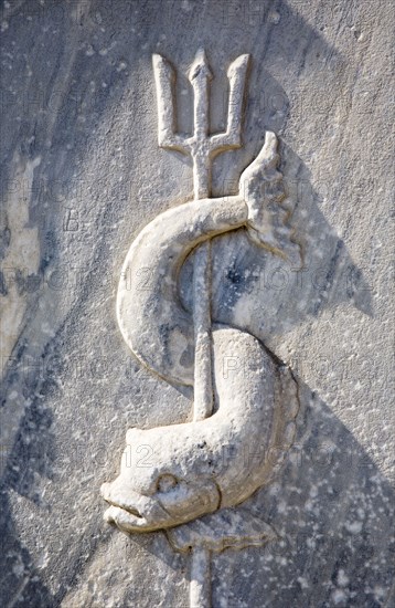 Athens, Attica, Greece. Close cropped view of stone carving of sea creature curved around trident. Greece Greek Attica Athens Europe European Vacation Holiday Holidays Travel Destination Tourism Ellas Hellenic Art Architecture Detail Carving Carved Stone Fish Trident Atenas Athenes Destination Destinations Ellada Southern Europe Water