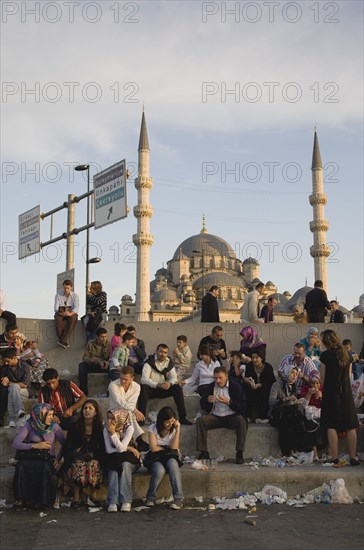 Istanbul, Turkey. Sultanahmet. Meeting place on steps in front of The New Mosque or Yeni Camii from the Galata Bridge. Mixed crowd many eating sitting amongst discarded rubbish with minarets and dome of mosque behind. Turkey Turkish Istanbul Constantinople Stamboul Stambul City Europe European Asia Asian East West Urban Destination Travel Tourism Sultanahmet New Mosque Architecture People C rowd Steps Minaret Minarets Dome Cultural Cultures Destination Destinations Middle East Order Fellowship Guild Club Religion Religious South Eastern Europe Turkiye Western Asia