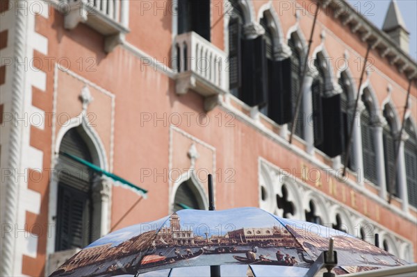 Venice, Veneto, Italy. Open umbrella printed with painting Return of the Bucentoro to the Molo on Ascension Day by Canaletto. Facade of the Hotel Danieli behind. Italy Italia Italian Venice Veneto Venezia Europe European City Hotel Danieli Facade Architecture Umbrella Parasol Painted Destination Destinations Southern Europe