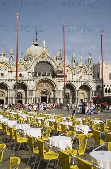 Venice, Veneto, Italy. Centro Storico St. Marks Square Cafe tables prepared for customers in early morning sunshine with facade of Basilica di San Marco behind. Italy Italia Italian Venice Veneto Venezia Europe European City Centro Storico St saint Mark Marks Square Cafe Cafes Restaurants Tables Chairs Yellow White Basilico San Marco Bar Bistro Blue Destination Destinations Religion Religious Southern Europe