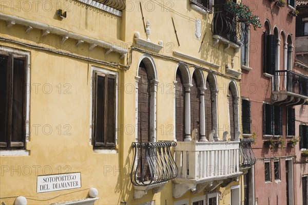 Venice, Veneto, Italy. Restored facades of canalside buildings painted pastel pink terracotta and yellow with window balconies and shutters in late summer sunshine. Italy Italia Italian Venice Veneto Venezia Europe European City Architecture Canal Yellow Balconies Exterior Facade Color Destination Destinations Southern Europe