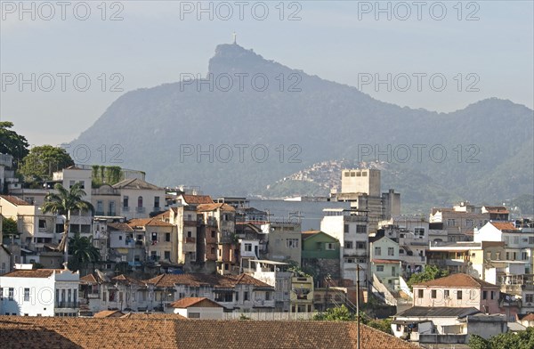 Rio de Janeiro, Brazil. Rooftops of Saude neighbourhood with a hillside favela or slum and the statue of Christ the Redeemer atop Corcovada mountain traditional tile roofs and palm trees. Brazil Brasil Brazilian Brasilian South America Latin Latino American City Urban Architecture Houses Housing Homes Favela Slum Corcovado Christ Statue Redeemer Saude Classic Classical Destination Destinations Historical Latin America Older Shanty South America Southern