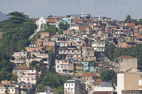 Rio de Janeiro, Brazil. Favela or slum housing above Saude neighbourhood some with traditional tile roofs very steep hill roads greenery and Church at left. Brazil Brasil Brazilian Brasilian South America Latin Latino American City Urban Architecture Houses Housing Homes Favela Favelas Slum Slums Saude Neighborhood Neighbourhood Classic Classical Destination Destinations Historical Latin America Older Shanty South America Southern