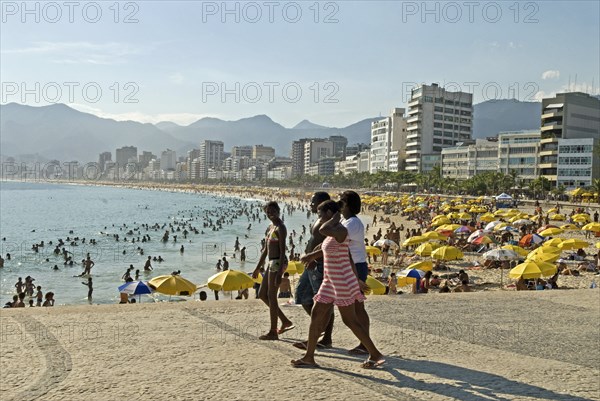 Rio de Janeiro, Brazil. Crowds at Ipanema beach with yellow umbrellas blue sea and sky swimmers in sea and hotels along the Avenue Vieira Souto with group of young women in foreground. Brazil Brasil Brazilian Brasilian South America Latin Latino American City Travel Destination Urban Vacation Beach Beaches People Sunbathing Crowds Childre Kids Young Ipanema Swimmers Swimming Hotels Sea Avenue Viera Souto Destination Destinations Female Woman Girl Lady Holidaymakers Immature Latin America Sand Sandy Beach Tourism Seaside Shore Tourist Tourists Vacation Sand Sandy Beaches Tourism Seaside Shore Tourist Tourists Vacation South America Southern Sunbather Water