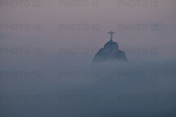 Rio de Janeiro, Brazil. The statue of Christ the Redeemer and the peak of Corcovado mountain above the cloud as dawn breaks over the city. Brazil Brasil Brazilian Brasilian South America Latin Latino American City Travel Destination Urban Vacation Statue Christ Redeemer Corcovado Color Destination Destinations Gray Latin America Religion Religious South America Southern