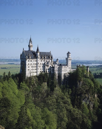 Fussen, Bavaria, Germany. Neuschwanstein Castle of King Ludwig on rocky hill. Germany German Euro Europe European Castle Hill View Fort History Kasteel Neush Beieren Schwanstein Duitsland Neuschwanstein King Ludwig Forest Trees perched Rock Outcrop Hill Bayern Blue Castillo Castello Color Destination Destinations Deutschland Gray History Historic Western Europe