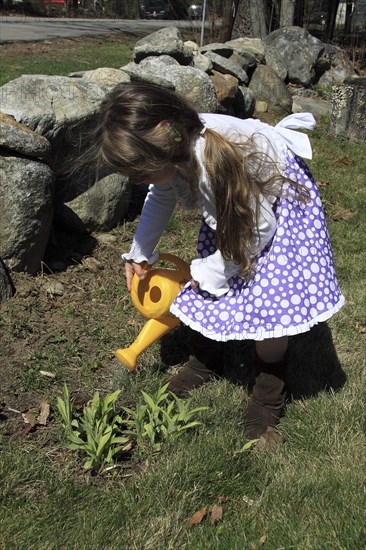 Young girl Kylan Stone waters plants in garden with a plastic watering can in Keene New Hampshire. Season Seasons Spring Springtime Children Child Young Girl Garden Gardening Chore Water Waters Watering Can Bucket Pour Pours Pouring Plant Plants Flora Green Yellow Plastic Keene New Hampshire NH USA MR Kylan Stone Model Release Model Released American Gardens Plants Immature Kids New Hampshire Live Free or Die Granite State North America Northern One individual Solo Lone Solitary United States of America