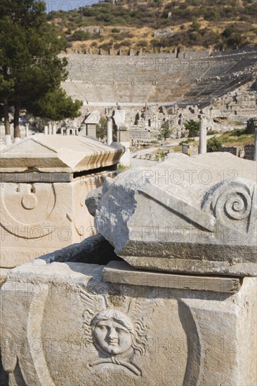 Selcuk, Izmir Province, Turkey. Ephesus. Masonry ruins with face carved in bas-relief and amphitheatre behind. Turkey Turkish Eurasia Eurasian Europe Asia Turkiye Izmir Province Selcuk Ephesus Ruin Ruins Masonry Rock Stone Carved Bas Relief amphitheatre Amphitheater Destination Destinations European History Historic Middle East South Eastern Europe Western Asia