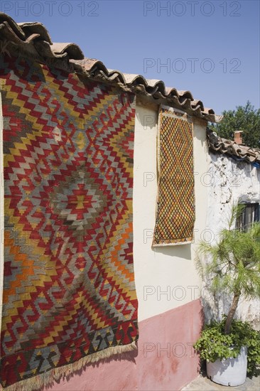 Selcuk, Izmir Province, Turkey. Kilim hanging up to dry in sun from wall of village house. Turkey Turkish Eurasia Eurasian Europe Asia Turkiye Izmir Province Selcuk Kilim Kilims Rug Rugs Carpet Carpets Hanging Roof Tiles Slates Destination Destinations European Middle East South Eastern Europe Western Asia