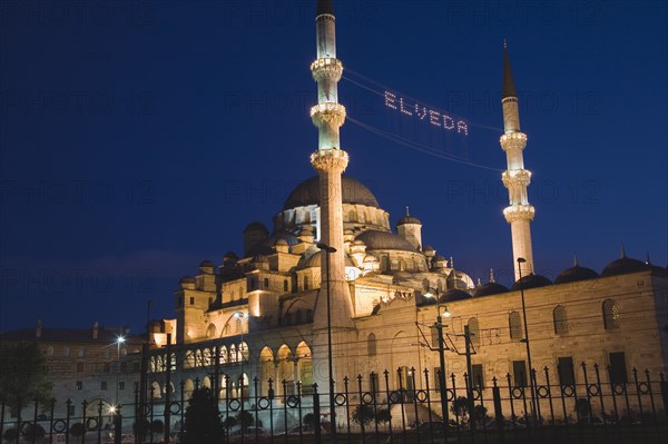 Istanbul, Turkey. Sultanahmet. The New Mosque or Yeni Camii at dusk with illuminated sign which reads Elveda meaning Go in Peace or Farewell to mark the end of Eid holiday hanging between the minarets. Seen from the Galata Bridge. Turkey Turkish Istanbul Constantinople Stamboul Stambul City Europe European Asia Asian East West Urban Destination Travel Tourism Sultanahmet New Mosque YYeni Camii Dusk Eid Elveda Sign Minaret Mionarets Muslim Mosle Islam Islamic Festival Illuminated Destination Destinations Middle East Moslem Nightfall Twilight Evenfall Crespuscle Crespuscule Gloam Gloaming Religion Religion Religious Muslims Islam Islamic Signs Display Posted Signage South Eastern Europe Turkiye Western Asia