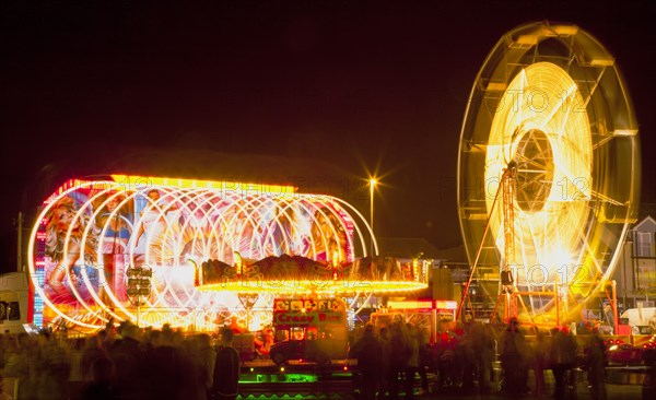 Lancing, West Sussex, England. Entertainment Funfairs Rides illuminated at night. England English UK United Kingdom GB Great Britain British Europe European West Sussex Lancing Funfair Rides Night Entertainment Leisure Color Colour Colorful Colourful Colored Coloured People Crowd Blur Blurred Ferris Wheel Big Neon Light