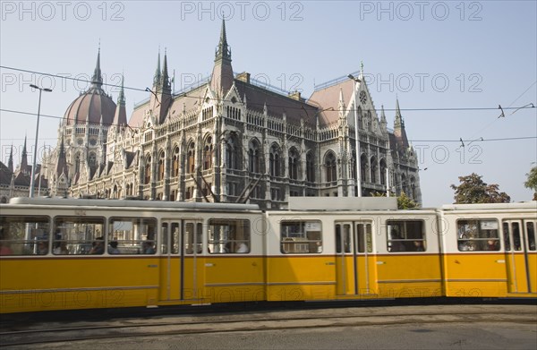Budapest, Pest County, Hungary. Yellow tram passing the Parliament Building. Hungary Hungarian Europe European East Eastern Buda Pest Budapest City Urban Transport Tram Parliament Building Architecture Electric Color Destination Destinations Eastern Europe Parliment