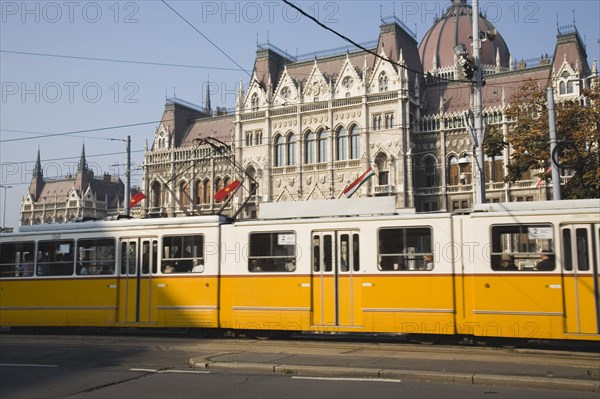 Budapest, Pest County, Hungary. Yellow tram passing the Parliament Building. Hungary Hungarian Europe European East Eastern Buda Pest Budapest City Architecture Building Building Urban Transport Tram Tram Color Destination Destinations Eastern Europe Parliment