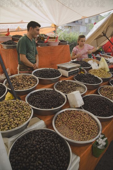 Kusadasi, Aydin Province, Turkey. Stall at weekly market selling olives and nuts with male stall holder and young girl standing behind display and set of electronic scales. Turkey Turkish Eurasia Eurasian Europe Asia Turkiye Aydin Province Kusadasi Market Markets Stall Display Olive Olives Dried Nut Nuts Scales Electronic Multi Muliple Color Colour Colors Colours Colored Coloured Destination Destinations European Immature Kids Middle East South Eastern Europe Western Asia