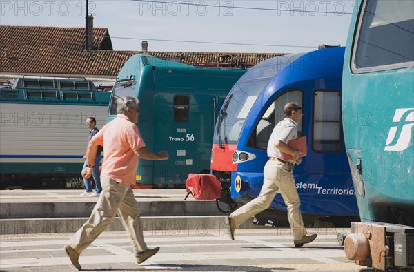 Venice, Veneto, Italy. Commuters running to board local train with regional trains on platforms at side. Italy Italia Italian Venice Veneto Venezia Europe European City Station Station Hurry Rush Platform Commuters Commute Travel Travel People Communications Railways Rail Trains Train Transport Destination Destinations Southern Europe