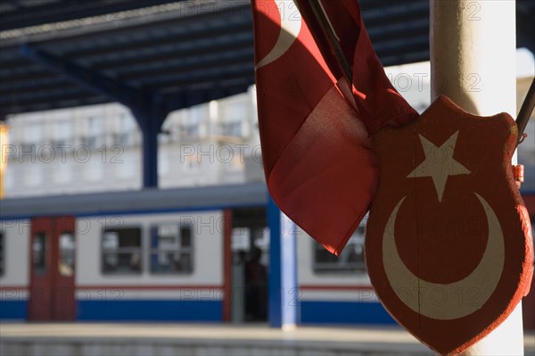Istanbul, Turkey. Sultanahmet. Istanbul Sirkeci Terminal Turkish flag and emblem in foreground with train at platform behind. Sirkeci is a terminus main station of the Turkish State Railways or TCDD in Sirkeci on the European part of Istanbul. International domestic and regional trains running westwards depart from this station which was inaugurated as the terminus of the Orient Express Turkey Turkish Istanbul Constantinople Stamboul Stambul City Europe European Asia Asian East West Urban Destination Travel Tourism Transportt Rail Railway Train Trains Station PlatformSirkeci TCCD Color Destination Destinations Middle East South Eastern Europe Turkiye Western Asia
