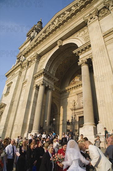 Budapest, Pest County, Hungary. Bride and groom greeting wedding guests on steps of Saint Stephens Basilica after service. Hungary Hungarian Europe European East Eastern Buda Pest Budapest City People Crowd Couple Wed Wedding Marriage Bride Groom White Dress Veil Flowers St Saint Stephen Stephens Basilica Church Exterior Blue Color Cultural Cultures Eastern Europe Marriage Marrying Espousing Hymeneals Nuptials Order Fellowship Guild Club Religion Religious