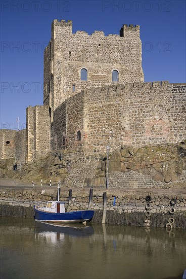 Carrickfergus, County Antrim, Ireland. Castle exterior with a boat moored in the foreground. Ireland Irish Eire Erin Europe European Ulster North Northern County Antrim Carrickfergus Castle Fortified Fortifications Old Stone Water Sea Harbour Port Boat Moored Blue Sky Castillo Castello Color Destination Destinations Gray History Historic Northern Europe Poblacht na hEireann Republic Water Castle Castello Castle Castillo Colour Grey