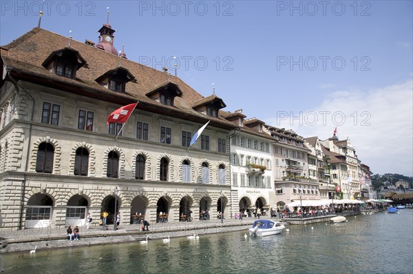 Lucerne, Switzerland. View along waterfront buildings toward thge Chapel Bridge. Switzerland Swiss Lucerne Chapel Wooden Bridge Water Urban Travel Tourist Tourists Europe European City Buildingts Architecture Swans Blue Sky Lucerna Luzern Destination Destinations Holidaymakers Schweiz Sightseeing Suisse Svizzera Tourism Western Europe