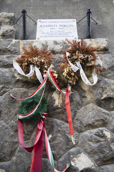 Budapest, Pest County, Hungary. Memorial to Holocaust victim Miklos Radnoti birth name Miklos Glatter 5 May 1909 to 10 November 1944 a Hungarian poet. With dried and freshly placed wreaths hung with coloured ribbon. Hungary Hungarian Europe European East Eastern Buda Pest Budapest City Memorial Stone Holocaust Miklos Radnoti Glatter Poet Wreath Flowers Ribbon Colored Cultural Cultures Destination Destinations Eastern Europe Five Order Fellowship Guild Club Ten