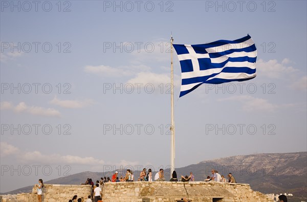 Athens, Attica, Greece. Acropolis Greek flag flying with tourists admiring view of the city. Greece Greek Europe European Vacation Holiday Holidays Travel Destination Tourism Ellas Hellenic Attica Athens Acropolis Flag Ruin Ruins Tourists Atenas Athenes Color Destination Destinations Ellada History Historic Holidaymakers Southern Europe