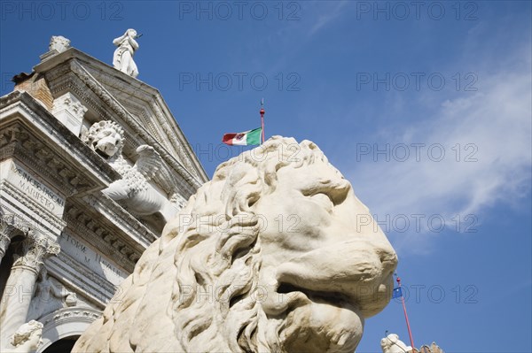 Venice, Veneto, Italy. Centro Storico Arsenale Castello with guardian lion statue in foreground and Italian tricolour flag against blue sky of late summer. Italy Italia Italian Venice Veneto Venezia Europe European City Sky Blue Statue Tricolor Tricolour Flag Arsenale Arsenale Centro Guardian Lion Castle Castillo Destination Destinations History Historic Southern Europe
