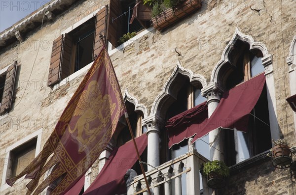 Venice, Veneto, Italy. Centro Storico Flag of the Republic of Venice depicting winged lion flies from facade with islamic influenced window arches. Italy Italia Italian Venice Veneto Venezia Europe European City Centro Storico Architecture Facade Flag Flags Republic winged Lions Window Windows Arch Arches Arched Destination Destinations History Historic Southern Europe