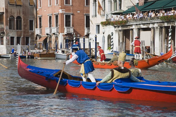 Venice, Veneto, Italy. Participants in the Regata Storico historical Regatta in brightly painted gondolas and wearing traditional costume approaching the Rialto bridge with onlookers on balconies of canalside buildings behind. Held each September teams represent Sestiere districts of Venice in traditional races. Italy Italia Italian Venice Veneto Venezia Europe European City Regata Regatta Gondola Gondola Gondolas Gondolier Boat Architecture Exterior Water Classic Classical Color Destination Destinations History Historic Holidaymakers Older Southern Europe Tourism Tourist