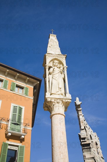 Verona, Veneto, Italy. Pastel painted facade of building with pale green painted window shutters and balconies with religious statue on free standing pillar in foreground against cloudless blue sky. Italy Italia Italian Veneto Verona Europe European City Sky Blue Christian Religion Religious Statue Shutters Shuttered Windows Window Exterior Exterior Facade Colourful Colorful Destination Destinations Religion Religious Christianity Christians Southern Europe