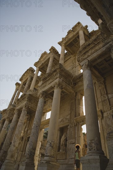 Selcuk, Izmir Province, Turkey. Ephesus. Roman Library of Celsus facade with young woman standing in doorway. Turkey Turkish Eurasia Eurasian Europe Asia Turkiye Izmir Province Selcuk Ephesus Ruin Ruins Roman Library Celcus Column Columns Facde Ancient Architecture Masonry Rock Stone Destination Destinations European Female Women Girl Lady History Historic Holidaymakers Immature Middle East One individual Solo Lone Solitary South Eastern Europe Tourism Tourist Western Asia