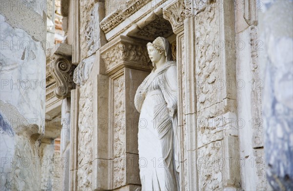 Selcuk, Izmir Province, Turkey. Ephesus. Damaged statue of female figure set in alcove of wall decorated with carvings in the antique city of Ephesus on the Aegean sea coast. Turkey Turkish Eurasia Eurasian Europe Asia Turkiye Izmir Province Selcuk Ephesus Ruin Ruins Roman Facde Ancient Architecture Masonry Rock Stone Statue Figure Destination Destinations European History Historic Middle East South Eastern Europe Water Western Asia