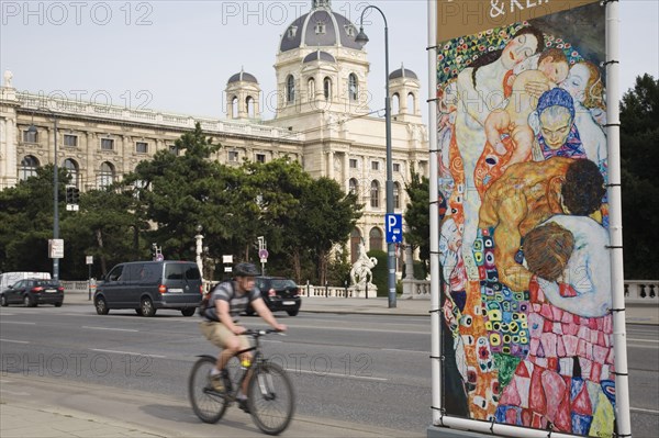 Vienna, Austria. Neubau District. Cyclist on Ringstrasse passing poster for the Leopold Museum featuring reproduction of the painting Death and Life by Gustav Klimt. Austria Austrian Republic Vienna Viennese Wien Europe European City Capital Neubau Distrgict Transport Bicycle Bike Cyclist Advert Advertisement Poster Gustav Klimt Rinstrasse Destination Destinations One individual Solo Lone Solitary Osterreich Viena Western Europe