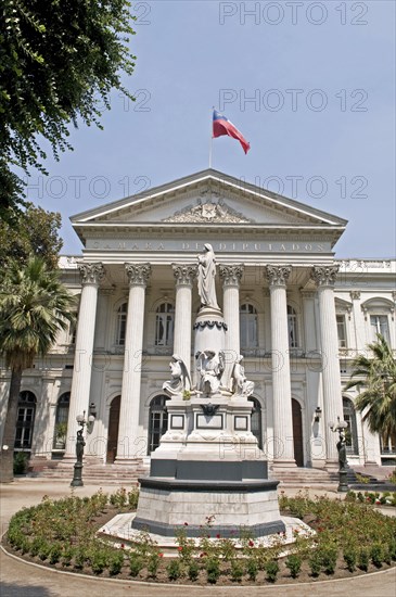 Santiago, Chile. Camara de Diputados Chamber of Deputies with Chilean flag flying on the building and ornamental religious statue in the foreground. Chile Chilean South America American Hispanic Santiago City Cityscape Urban Travel Destination Vacation Holiday Camara de Diputados Chamber Deputies Flag Statue Columns Destination Destinations Latin America Latino Religion South America Southern