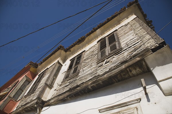 Kusadasi, Aydin Province, Turkey. Angled part view of exterior facade of Ottoman era whitewashed plaster and wooden house in the old town in late afternoon sunshine against cloudless blue sky. Turkey Turkish Eurasia Eurasian Europe Asia Turkiye Aydin Province Kusadasi Architecture Destination Destinations European Middle East South Eastern Europe Western Asia